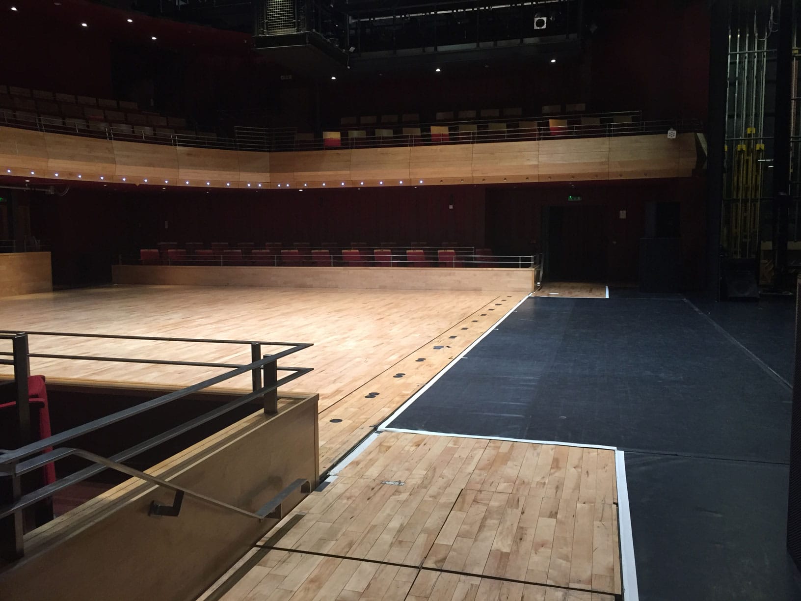 The Pentland Theatre in flat floor mode, taken from next to the stage - a large wooden floor with red theatre seats visible on two levels. On the right of the image is the black floor of the stage.