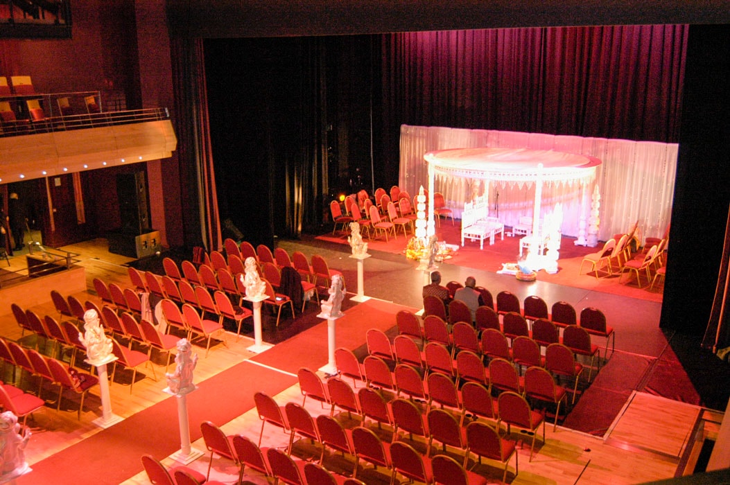 The Pentland Theatre set for an Indian Wedding with rows of red seating, a red carpet and a white curtain, seats and canopy on stage.