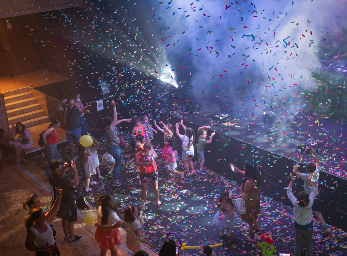 Adults and children dance under falling confetti