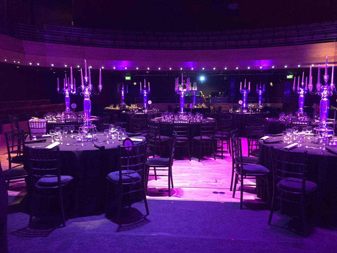 The Pentland Theatre set for a banquet with round tables covered in black table cloths with large silver candelabra.