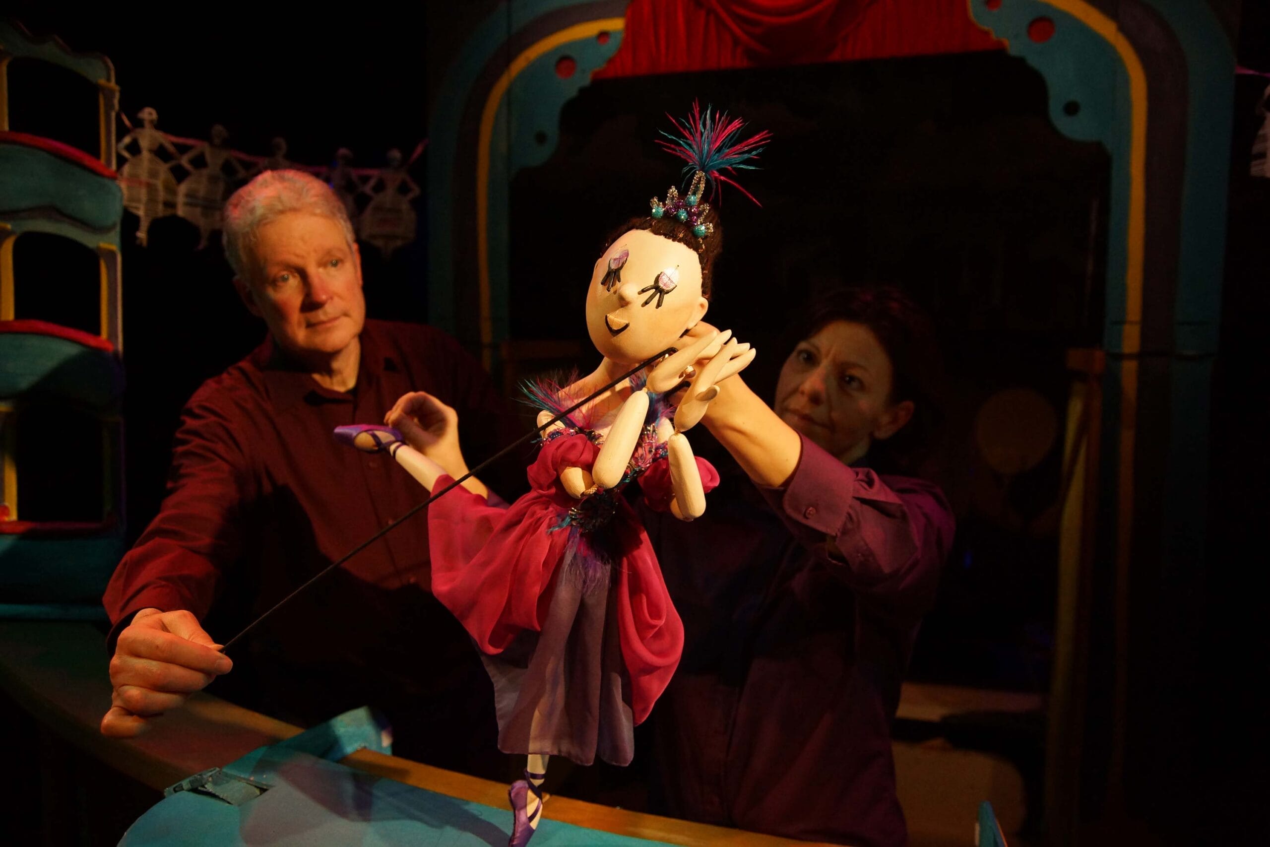 Two puppeteers hold a wooden ballerina puppet as she gracefully balances on one leg