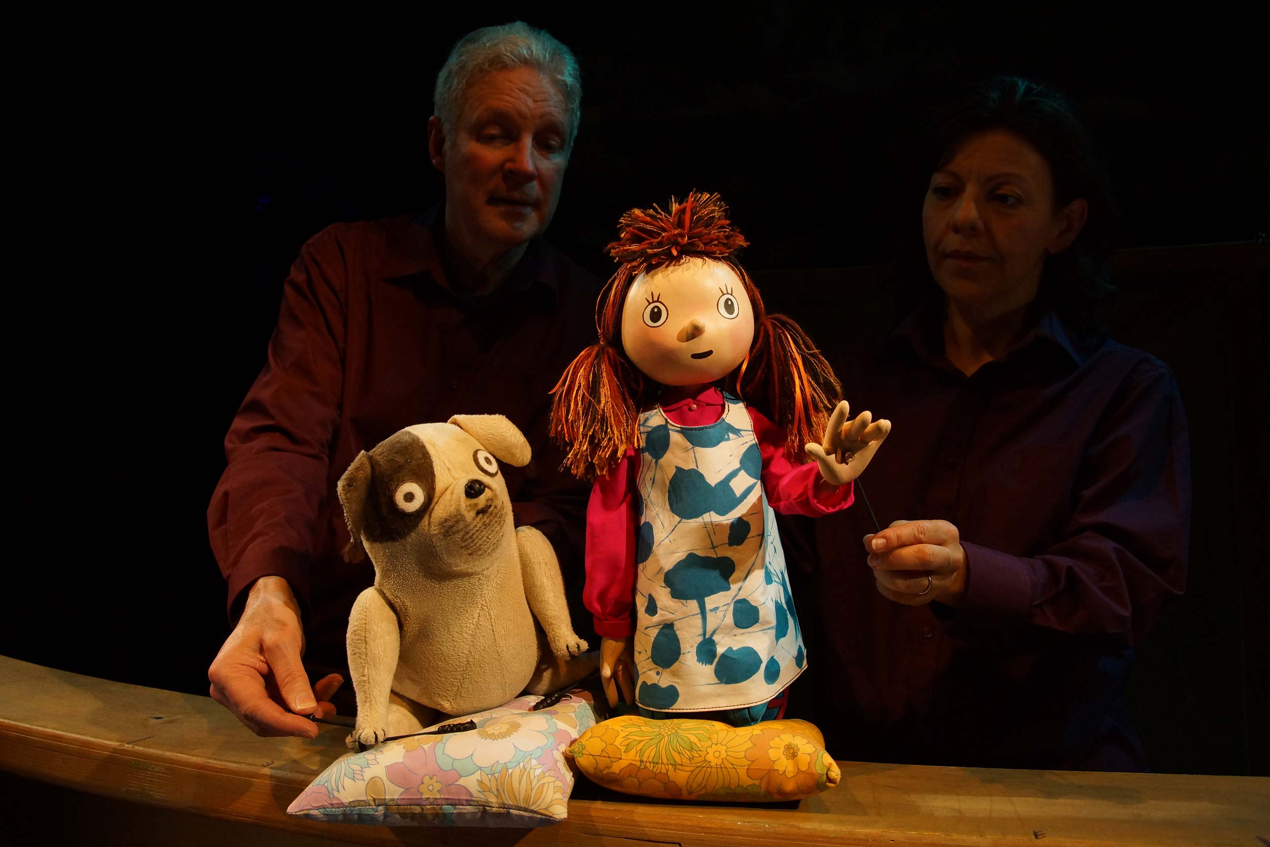 Two puppeteers hold puppets of Biff, a small dog, and Anna, a small girl.