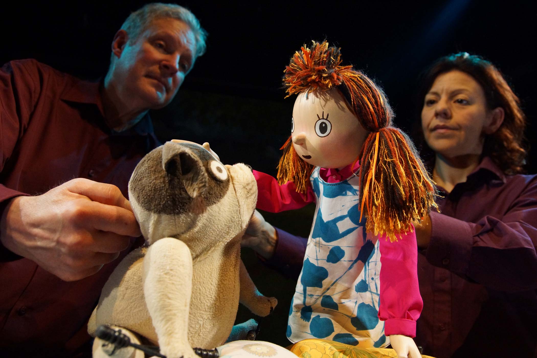 Two puppeteers hold puppets of Biff (a small dog) and Anna (a small girl) who are looking at eachother