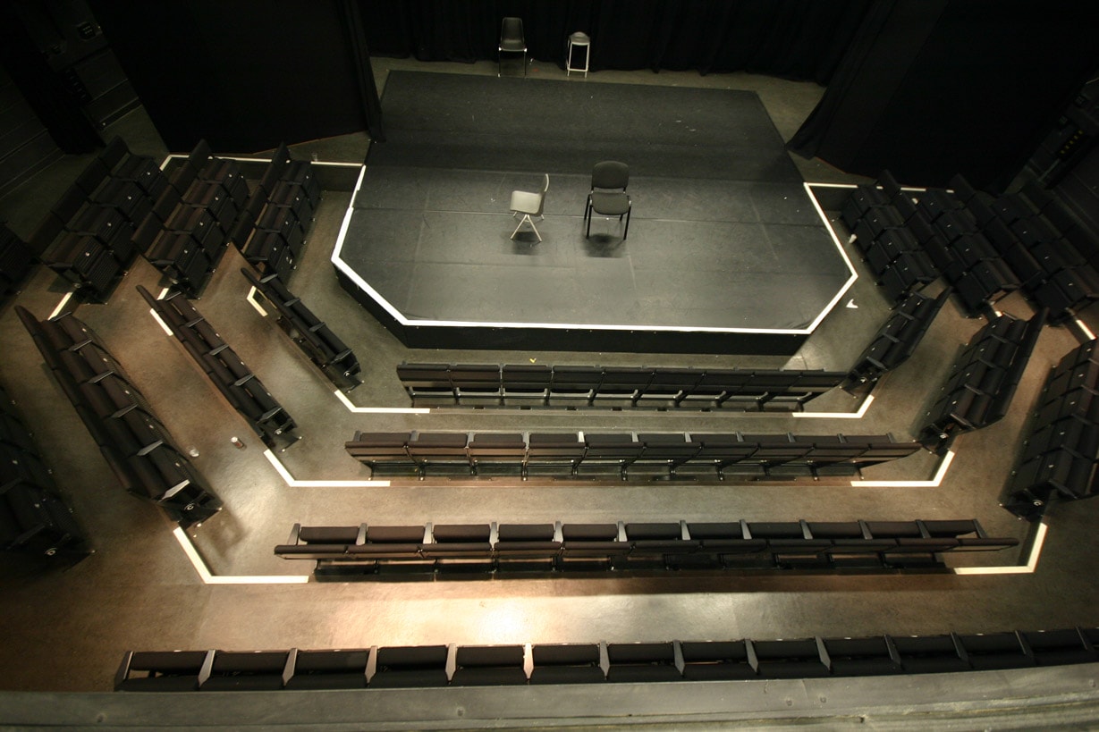 The Studio Theatre pictured from above. The space has a small thrust stage surrounded by rows of grey upholstered seats.