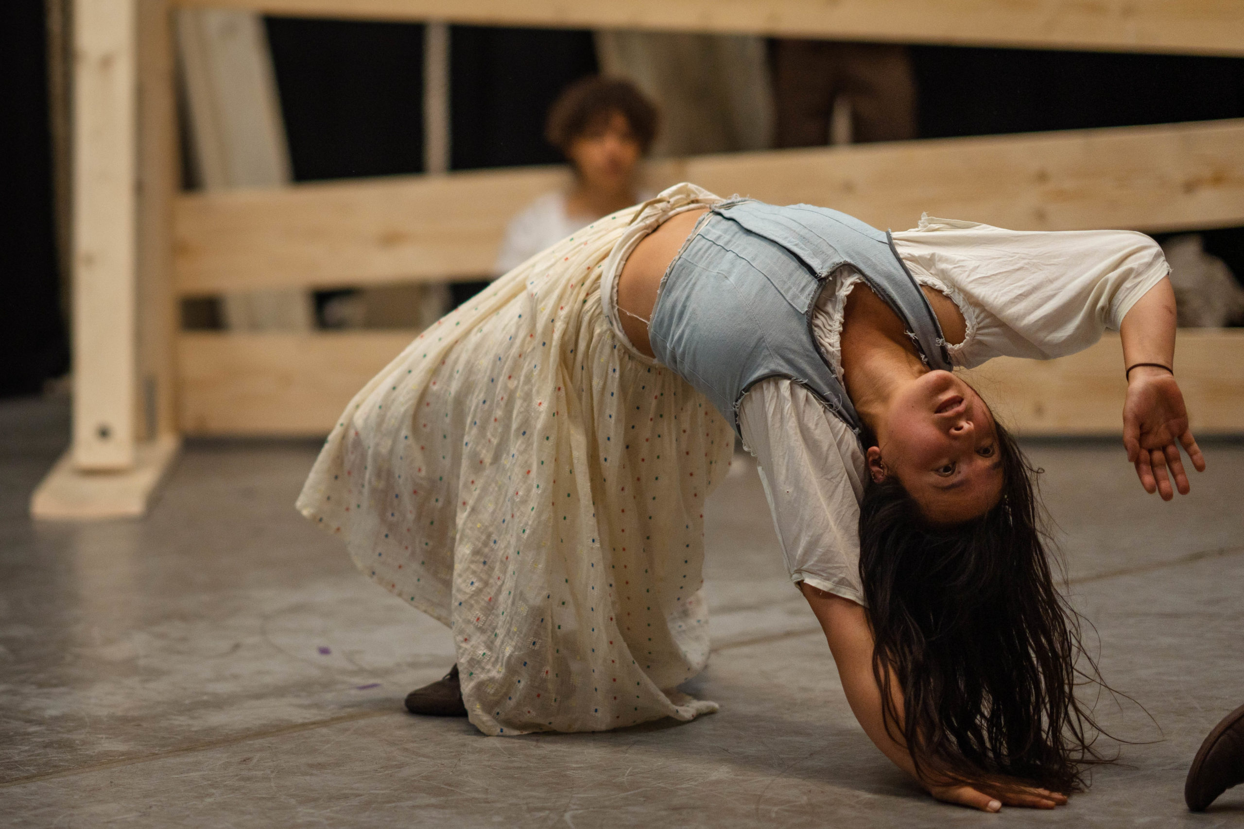 Rehearsal photography for a circus show. A performer exhibits a backbend. She has long dark hair and a flowing skirt.
