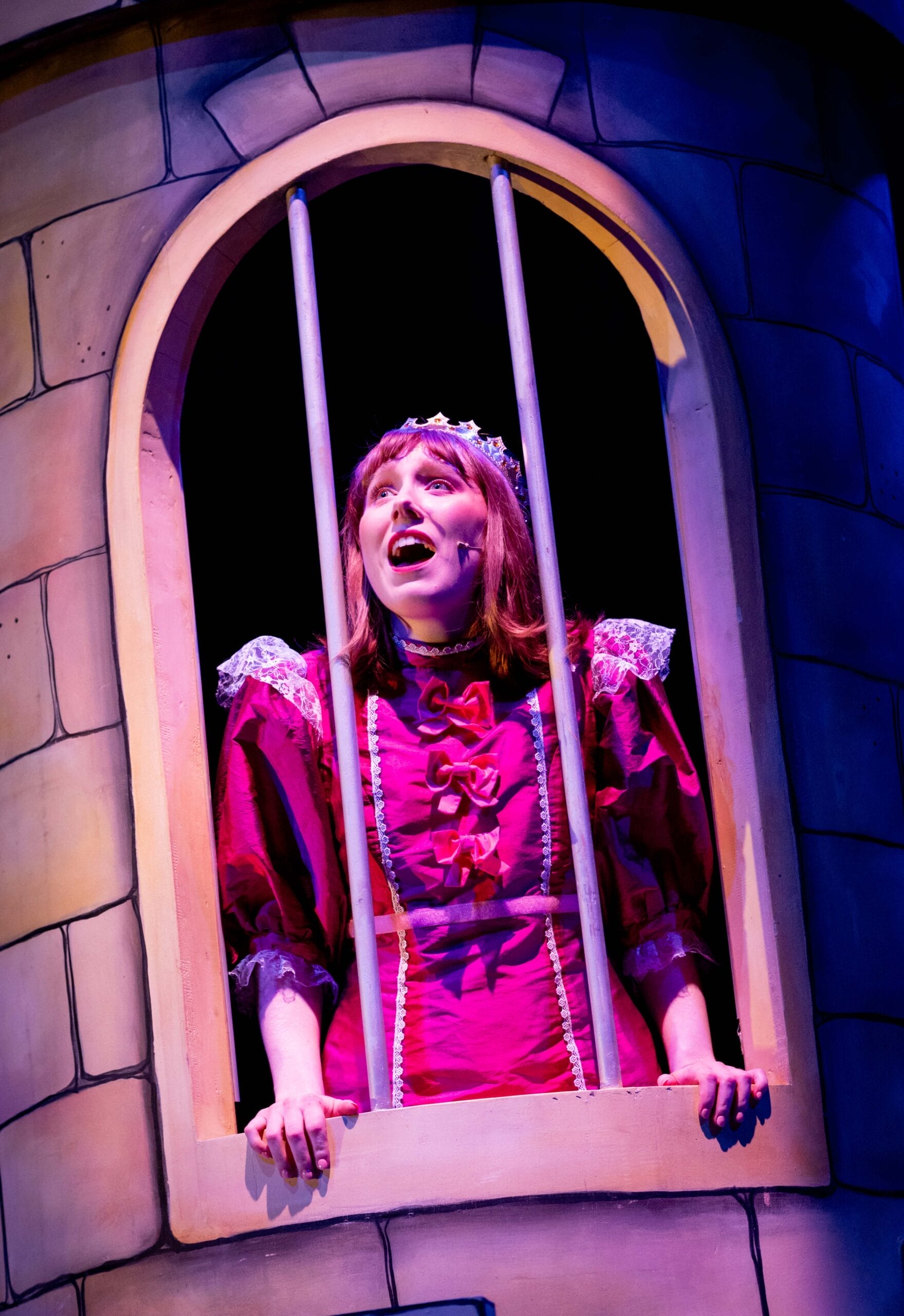A princess in a castle tower leans on the edge of a barred window. She is looking upwards and singing.