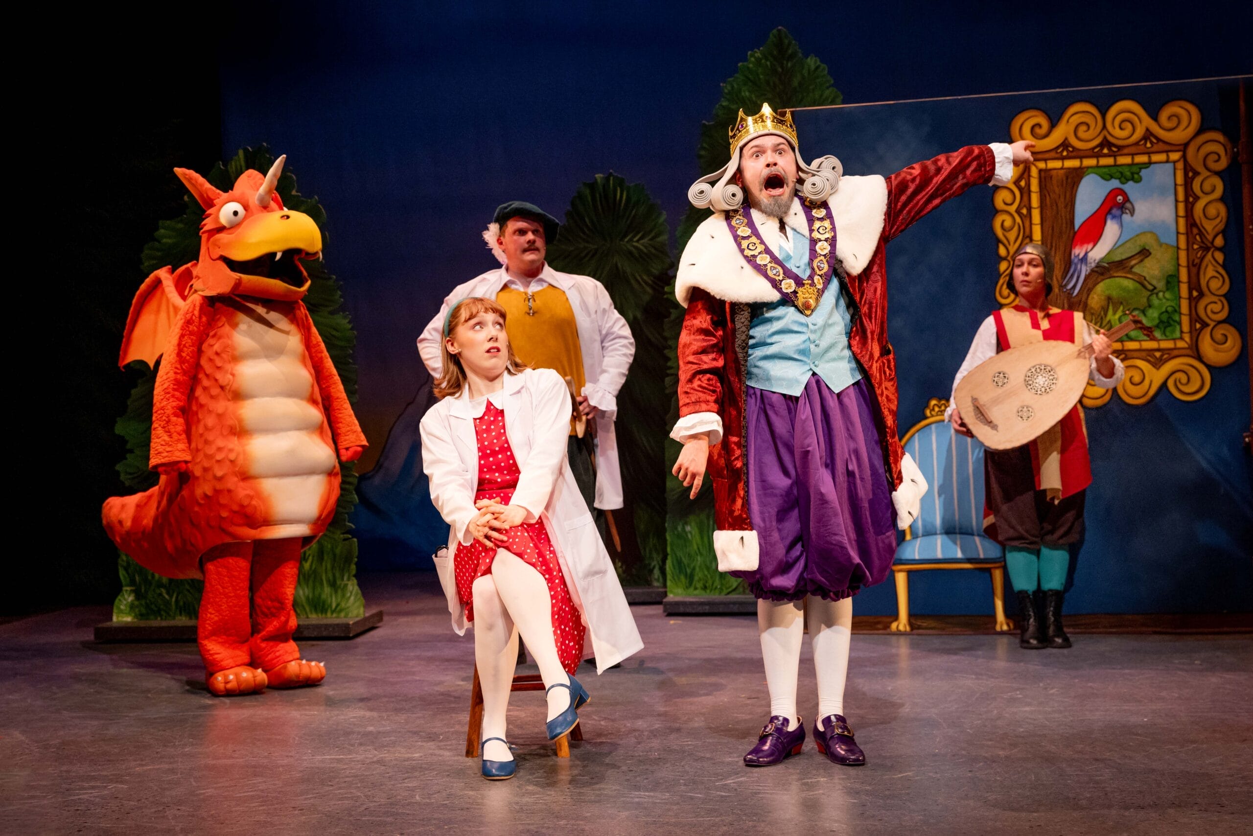 The king, in full regal regalia is shouting and is pointing to the right. Next to him is seated the princess dressed in a lab coat. The orange dragon Zog stands on the left and a lute player is on the right. Another scientist can be seen at the back of the stage.