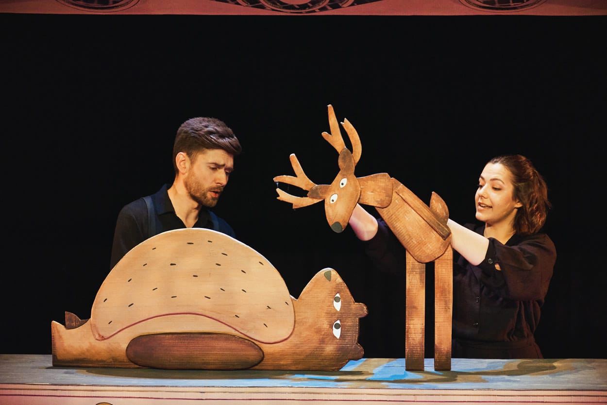2 performers on stage in I Want My Hat Back Trilogy holding cardboard puppets of a bear and a moose.