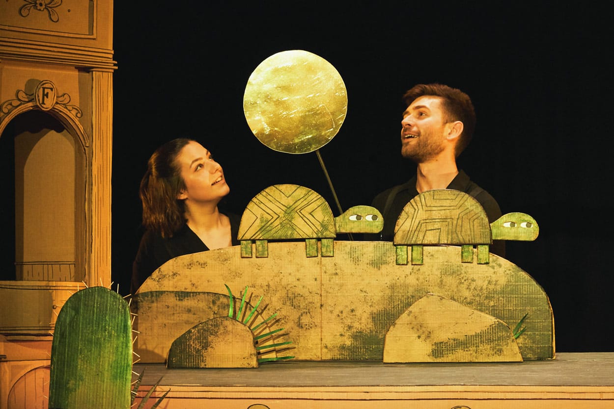 2 performers on stage in I Want My Hat Back Trilogy holding cardboard puppets of turtles.