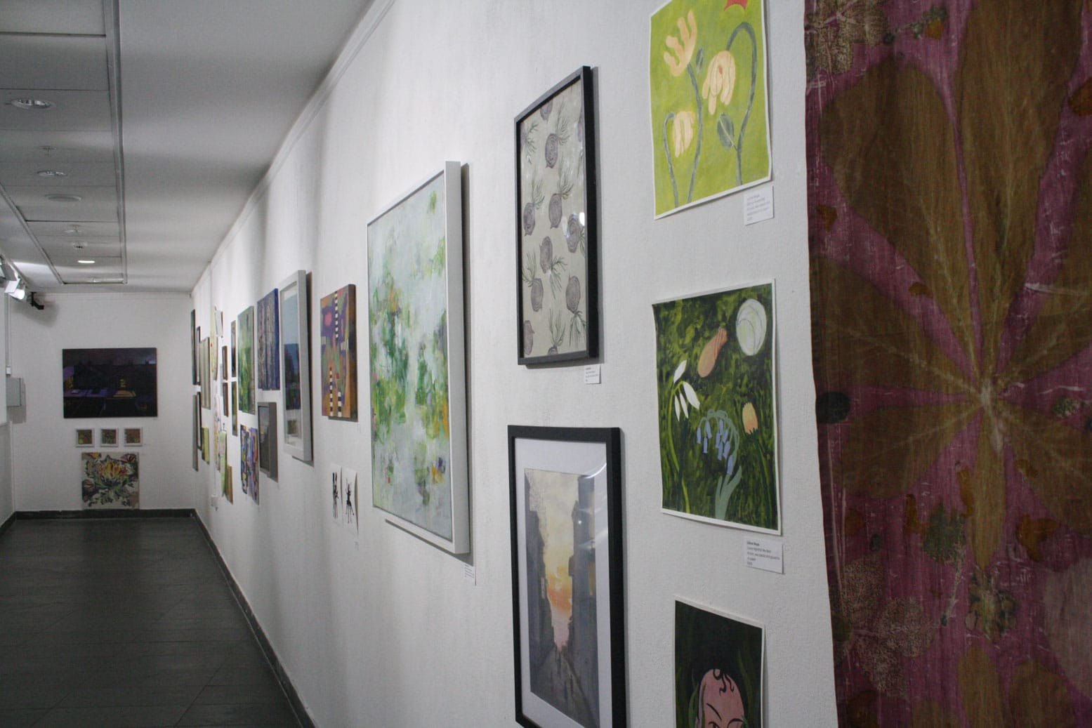 An exhibition on the Exhibition Wall. A white-washed wall with a variety of framed artworks.