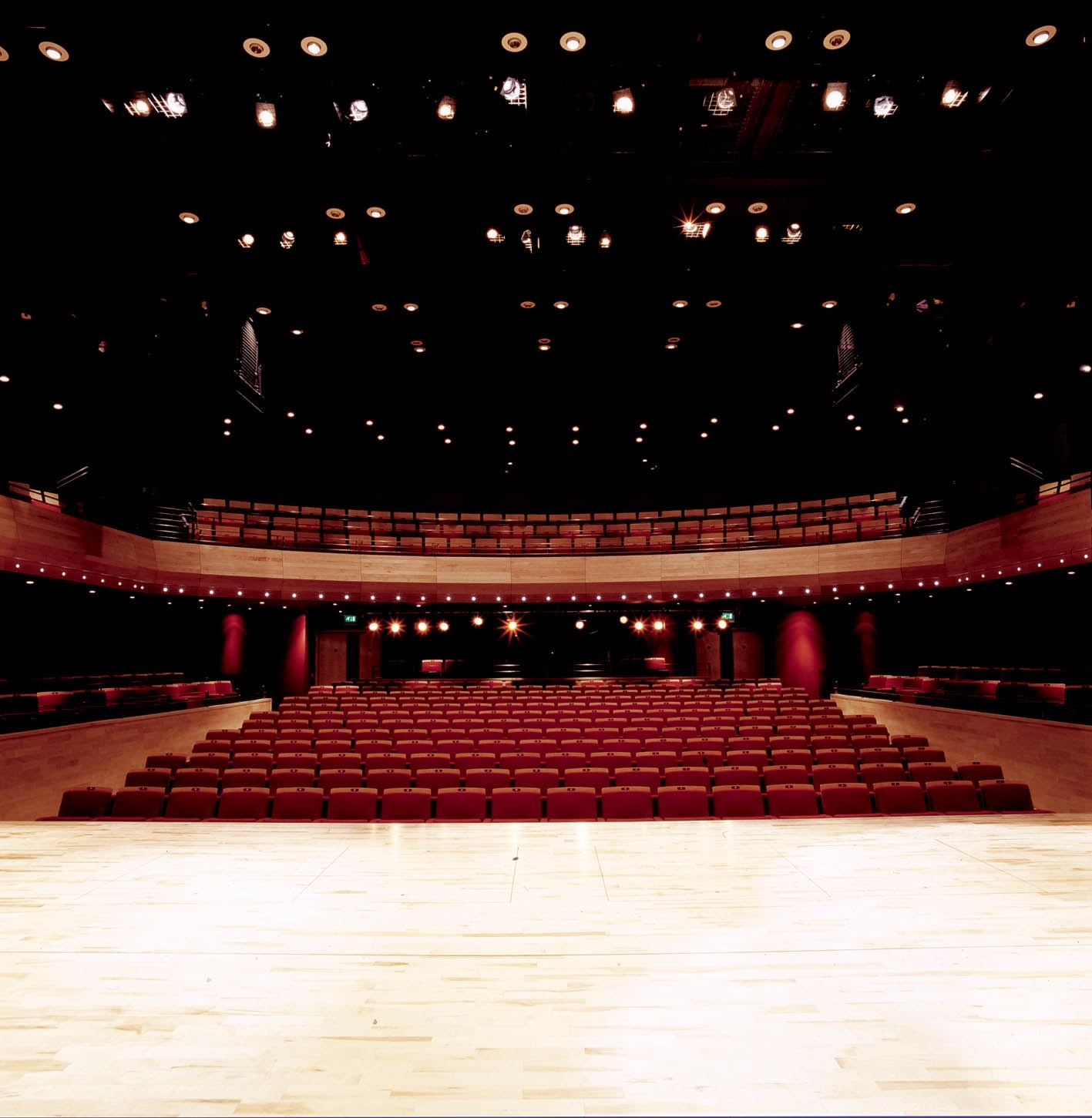 an image of the Pentland Theatre taken from the stage. The red seats of the stalls and balcony can be seen, and stage lights in the ceiling.