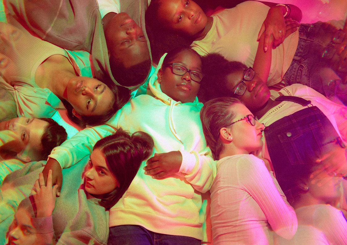A group of eight young people lying with their heads close together, pictured from above. The image is slightly blurred in places and the colours are slightly odd, as if it is a badly developed photo.