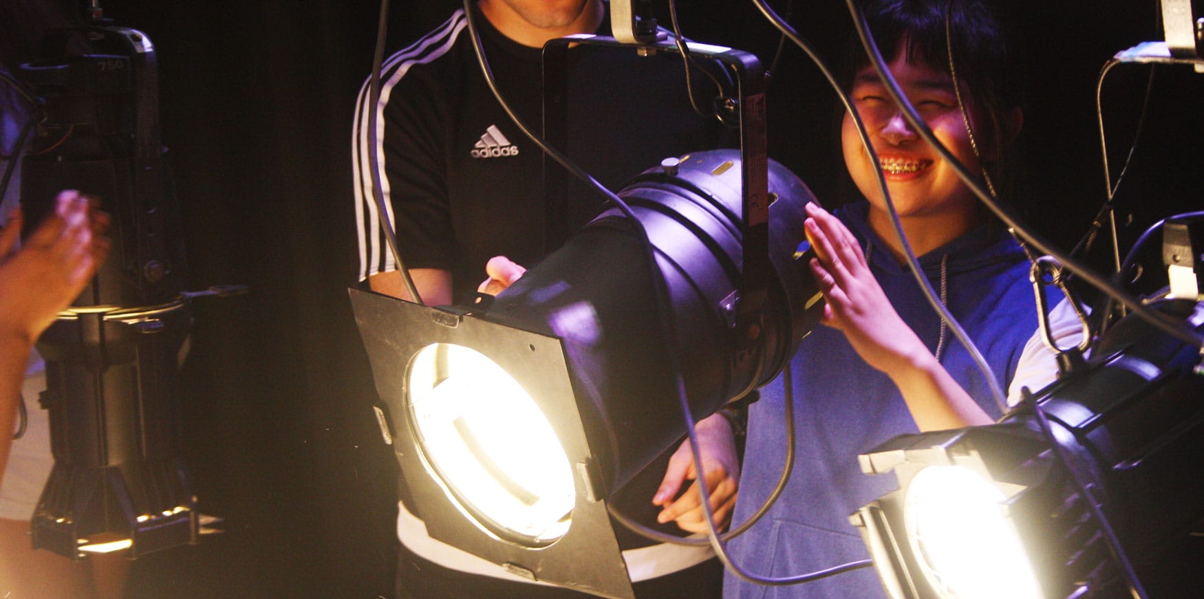 A work experience student, smiling broadly, repositions a stage light.