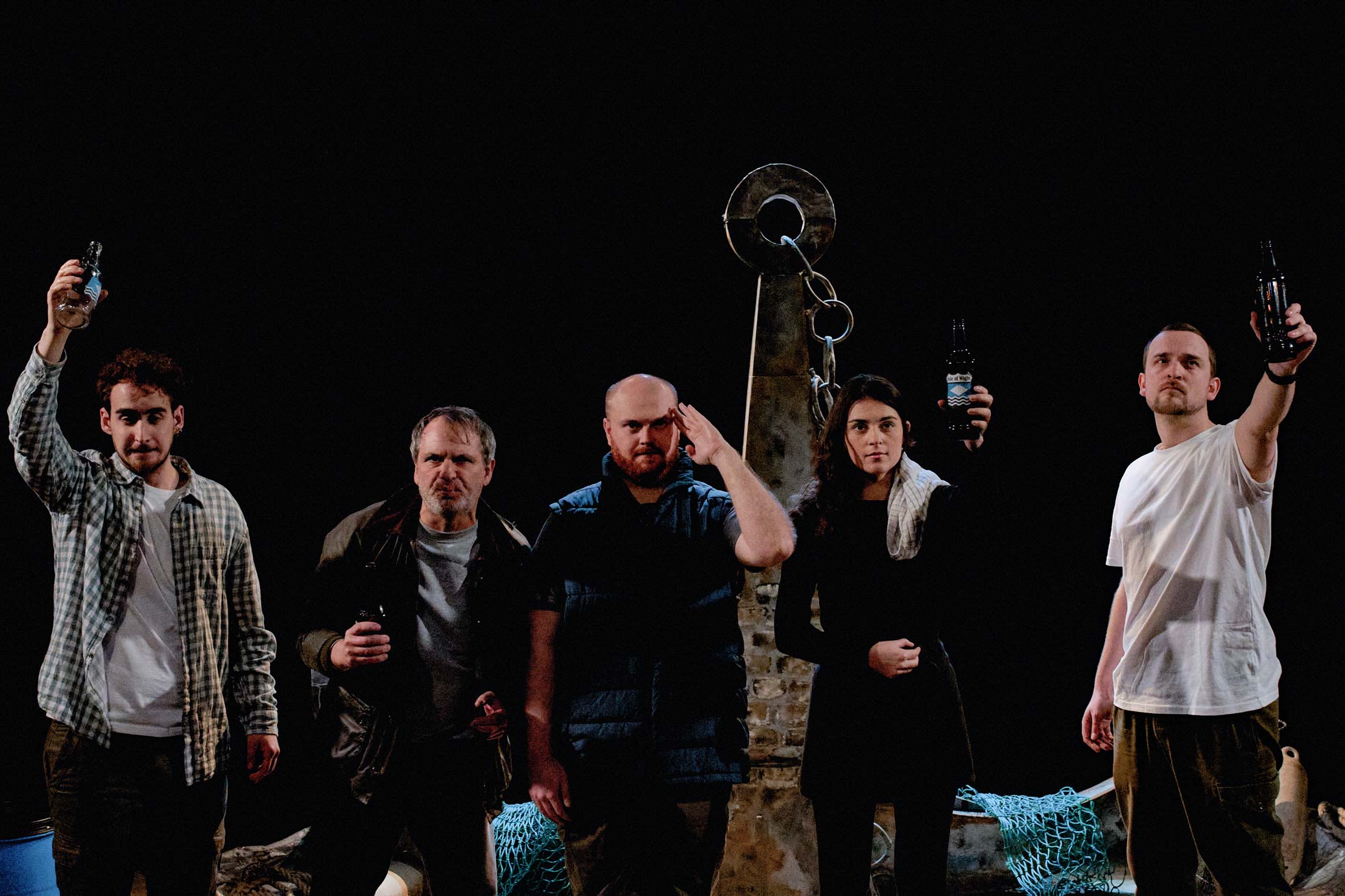 Five performers on stage in The Freshwater Five - they stand in a line, one salutes while others raise bottles of beer in a toast.