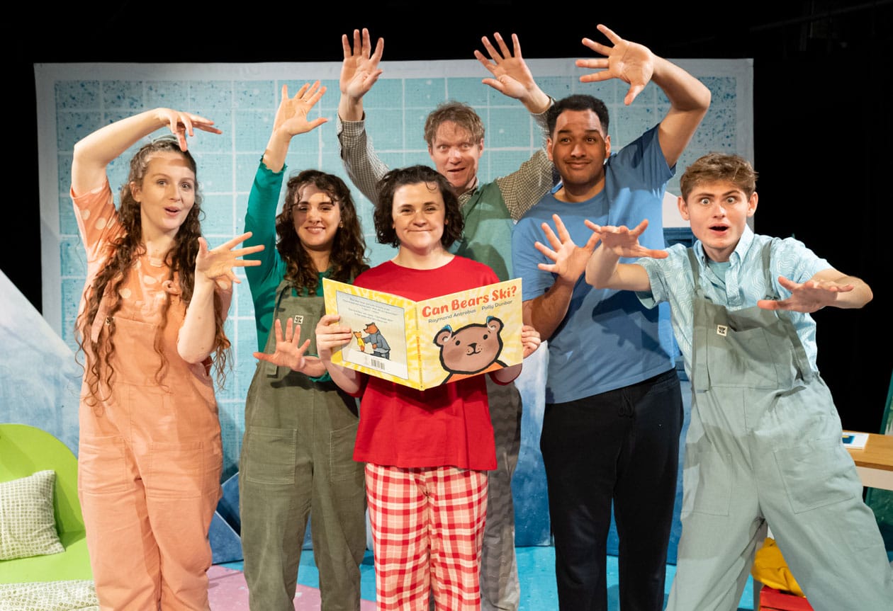 Six performers on stage with their arms in the air. One performer is holding the book Can Bears Ski?