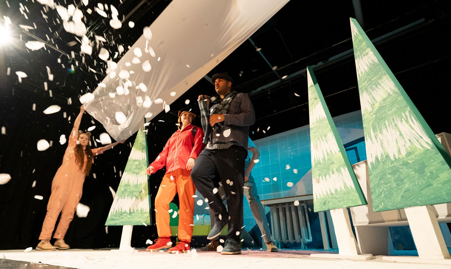 Two performers on stage in a snowy landscape. Snow flutters from above.