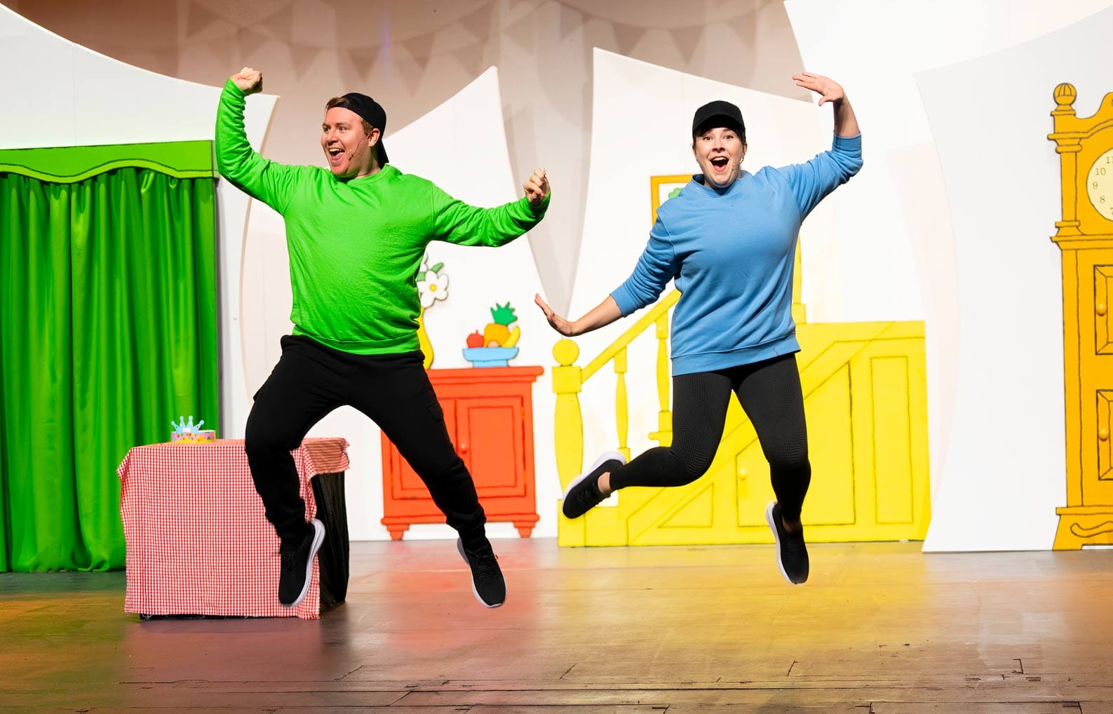 Two of the characters in the show are captured joyfully mid jumping. One is wearing green and the other is in blue.