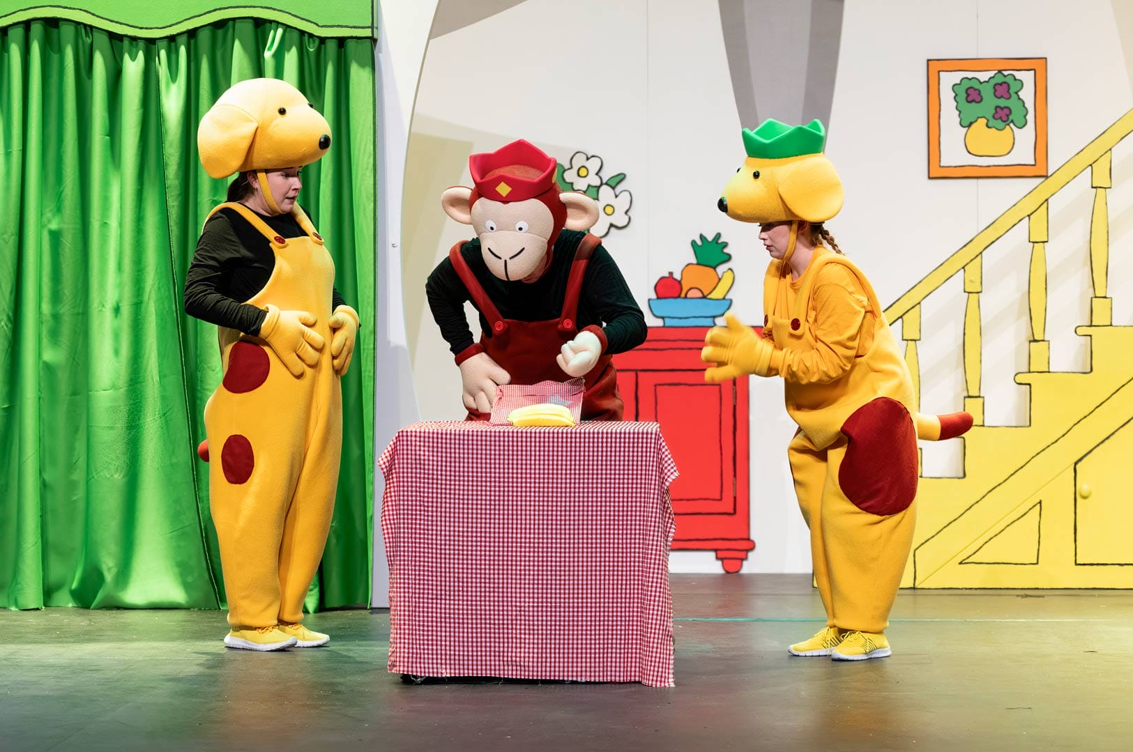 The monkey and spots are looking at the bananas on the kitchen table on stage.