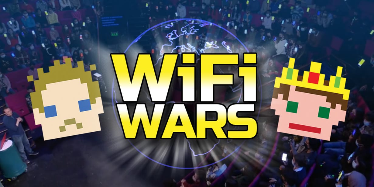 Bold yellow text reads WiFi WARS. Either side of the text, cartoon faces are rendered in pixel-style. One face wears a crown. The background is a blue toned photograph, depicting a previous Wifi Wars show in a theatre, with a full audience.