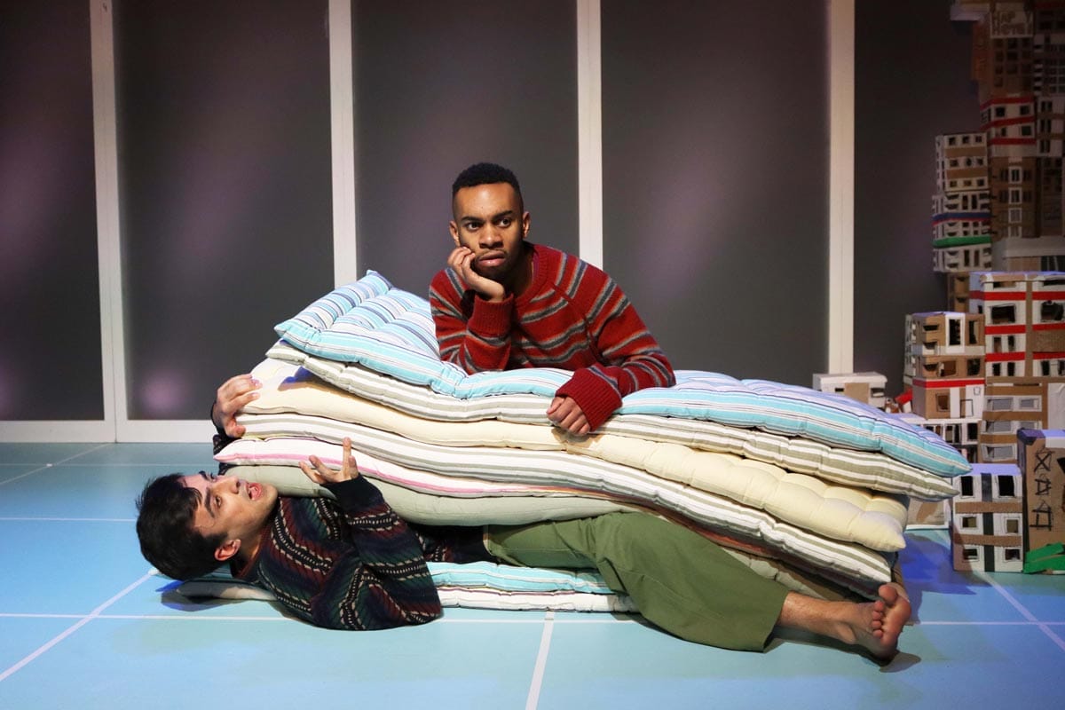 One of the male character resting on a pile of mattresses, stacked on top of the other male character.
