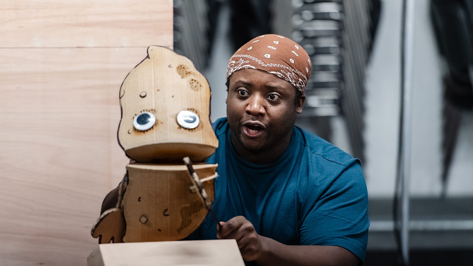 A performer holds a large cardboard puppet of a poo with large googly eyes.