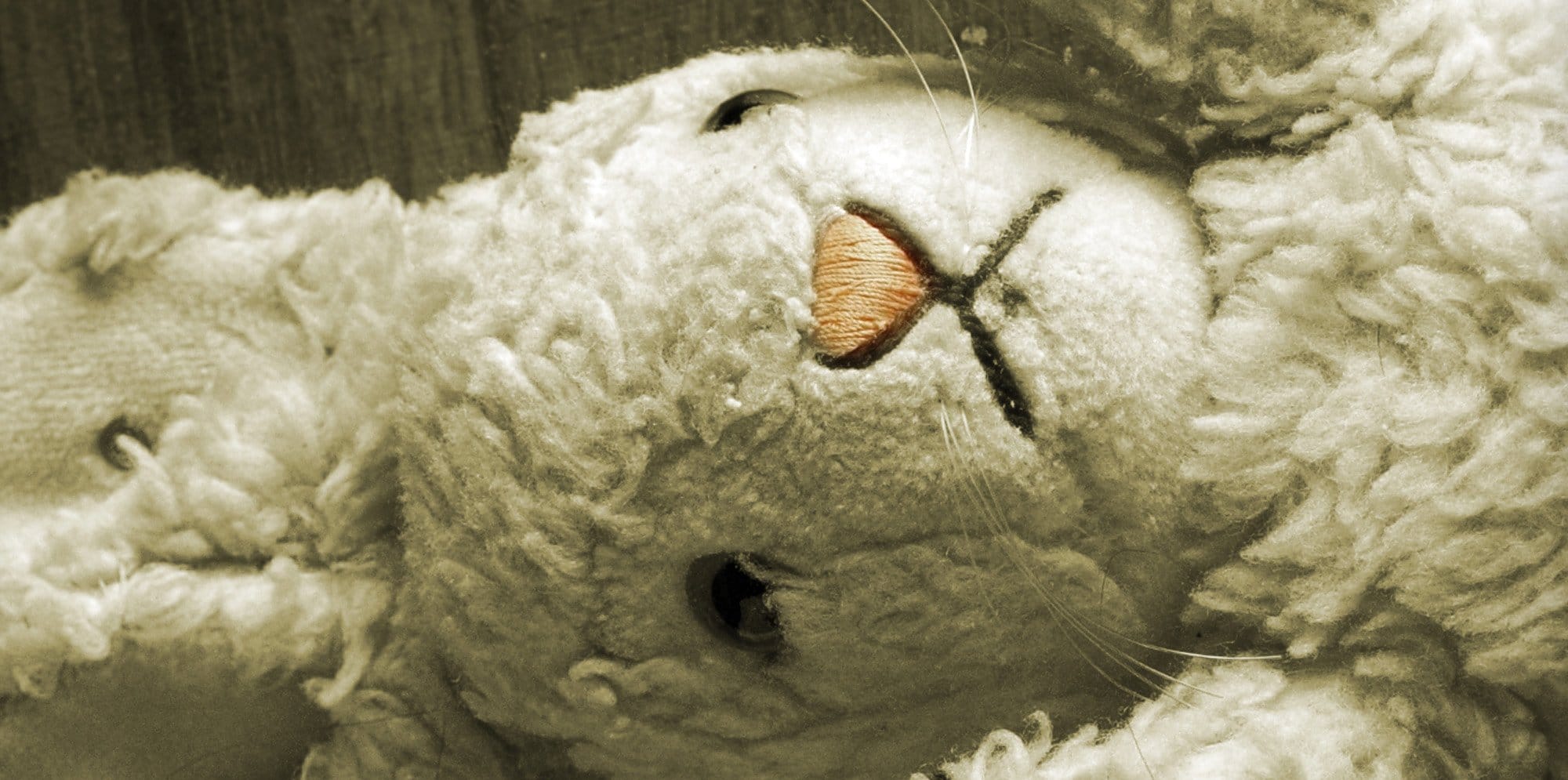 A white stuffed rabbit toy lays sideways on a wooden background. The image has a dulled sepia tone.