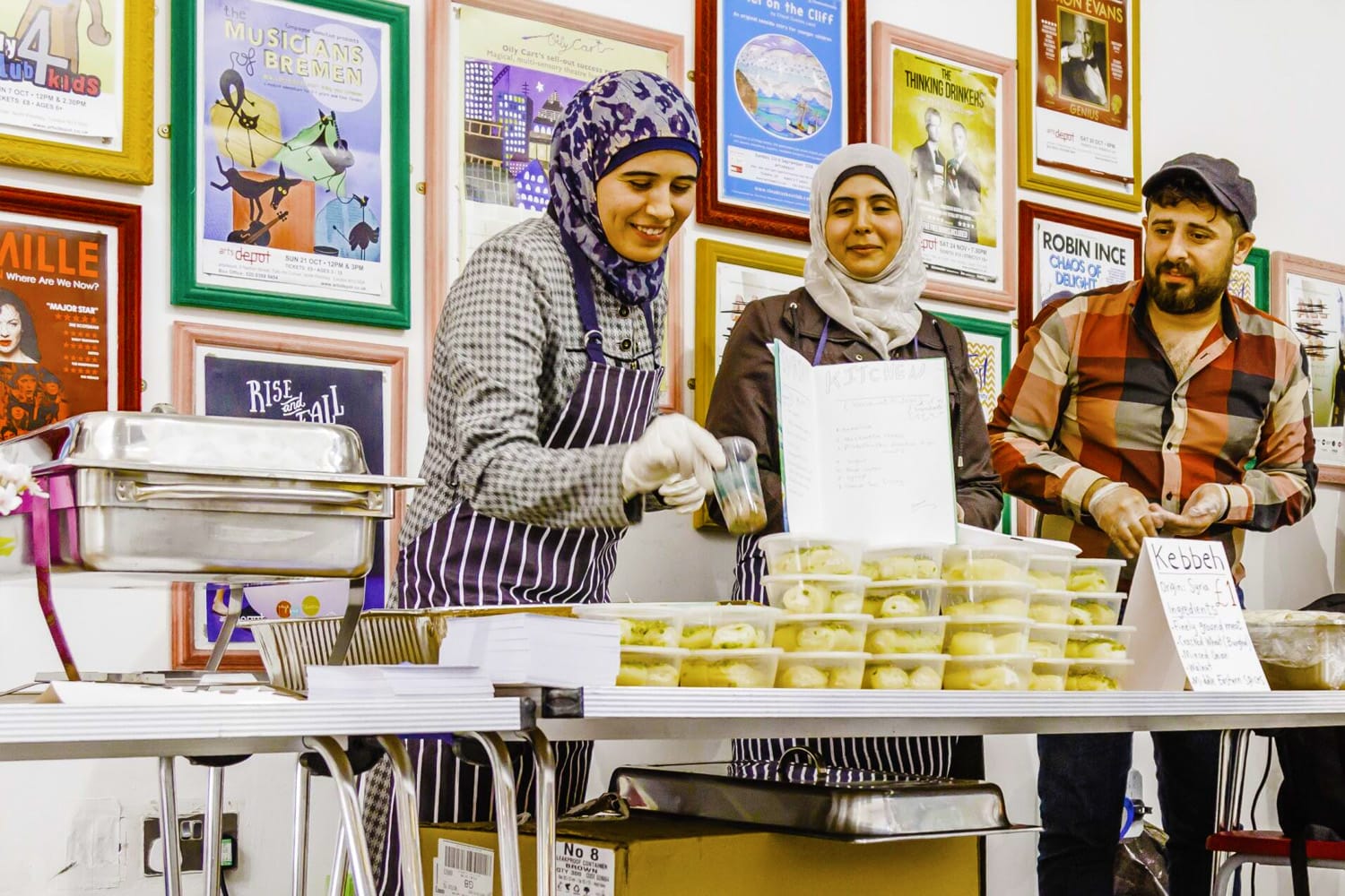Community vendors host a Syrian food tasting stall at an artsdepot event. The vendors smile together and attend to the food.