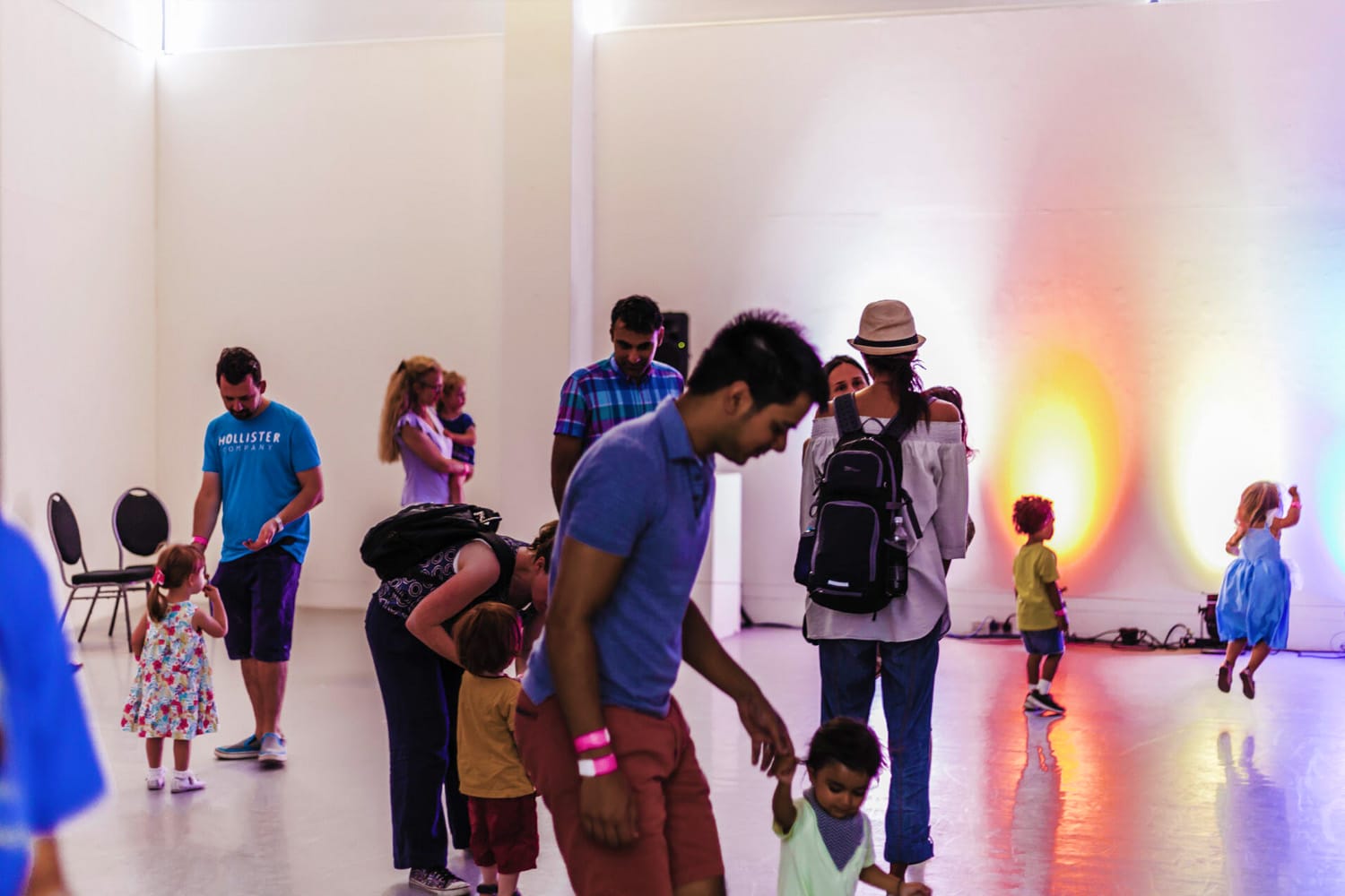 Several families are dancing together in an open space where brightly coloured lights are projected onto the walls.