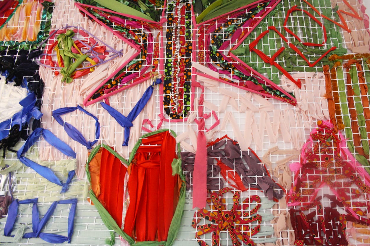Close up of a vibrant community tapestry made with recyclable materials in pinks reds and greens.