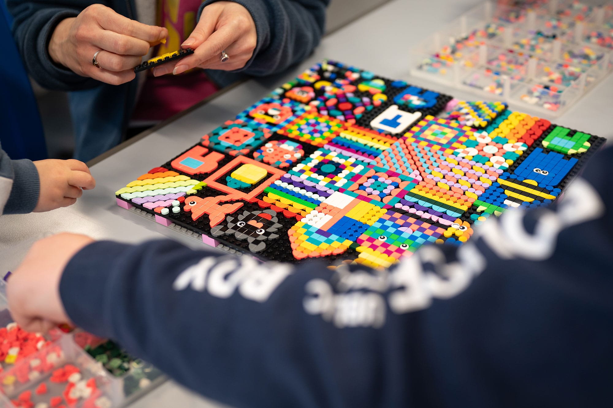 A high quality photo of a mosaic building workshop. Two participants are working on a mosaic of colourful plastic beads in various intricate patterns.