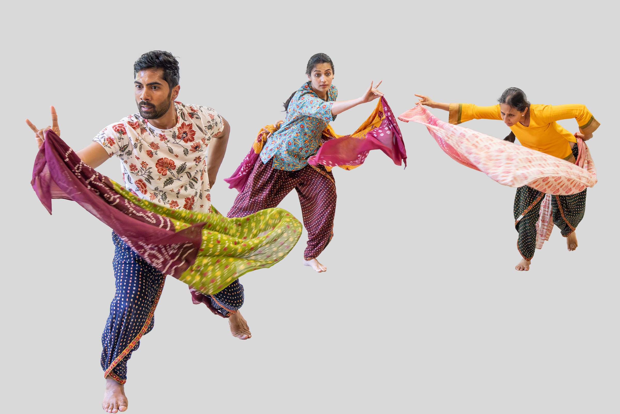 Three Desi performers pose against a white background, holding up colourful silk scarves in purples, greens and pinks.