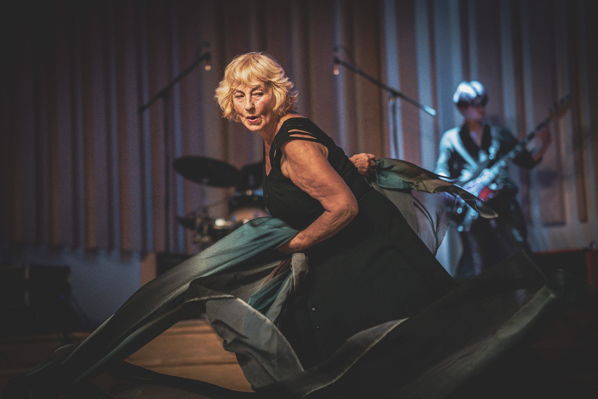 A older female dancer performs on stage with dark turquoise silks in dynamic motion.