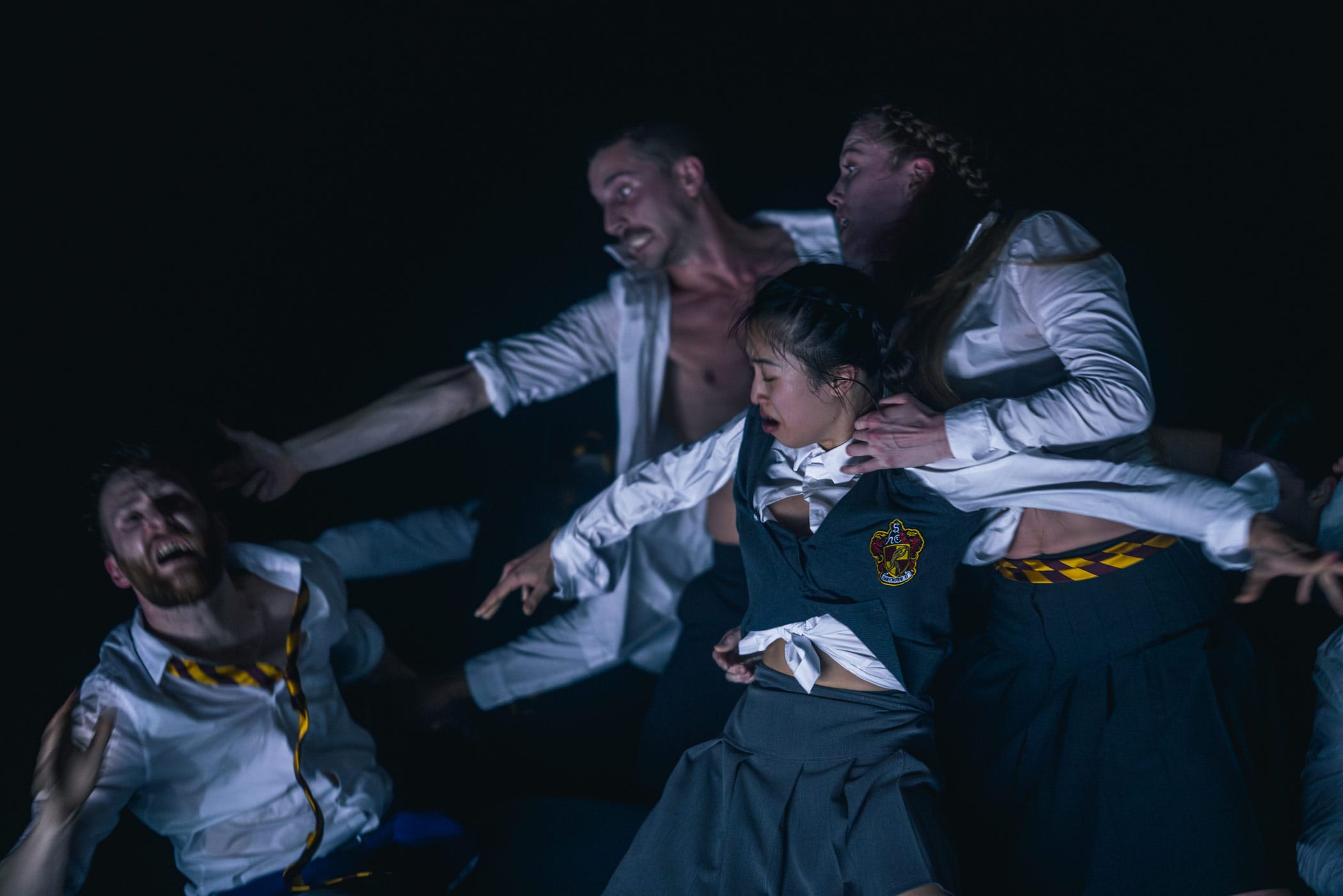 The ensemble performers are captured in the midst of conflict in school uniforms under a cold blue light.