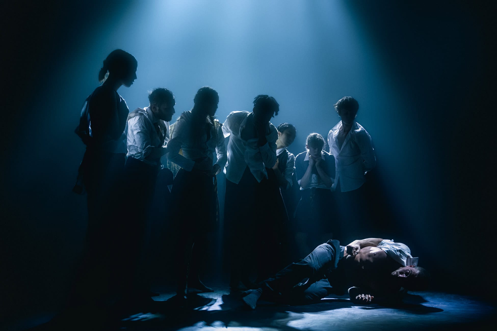 The silhouette of the performers shadow over one of the performers laid on the floor in the spotlight.