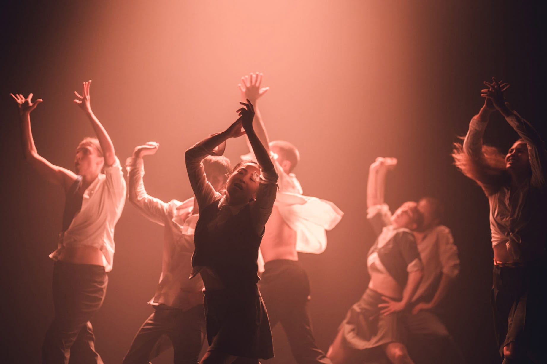 The ensemble dancers are each captured in motion, displaying different positions under a warm red light.