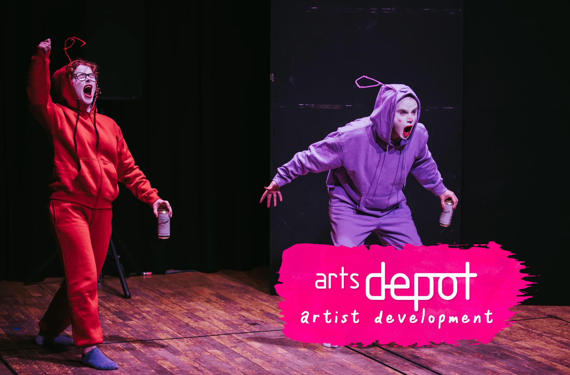 Two performers are dressed as alternative teletubbies in colourful tracksuits, with drag and clown inspired make-up. They are posing with dynamic expressions. In the bottom right-hand corner, a pink paint stroke logo reads 'artsdepot artist development'.