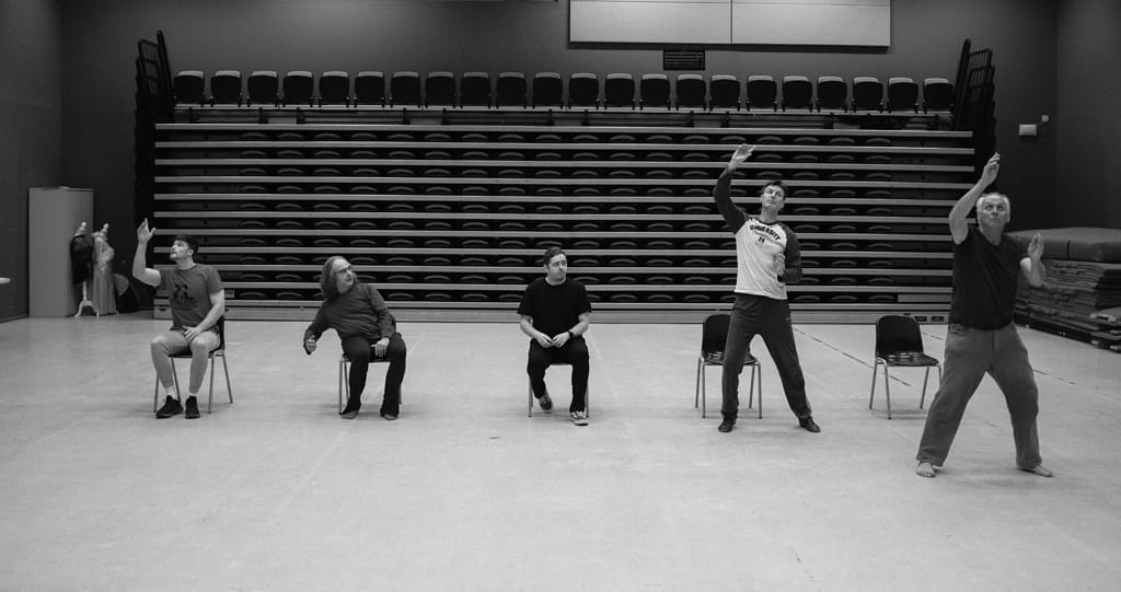 A black and white photo of five seated and standing men dancing.