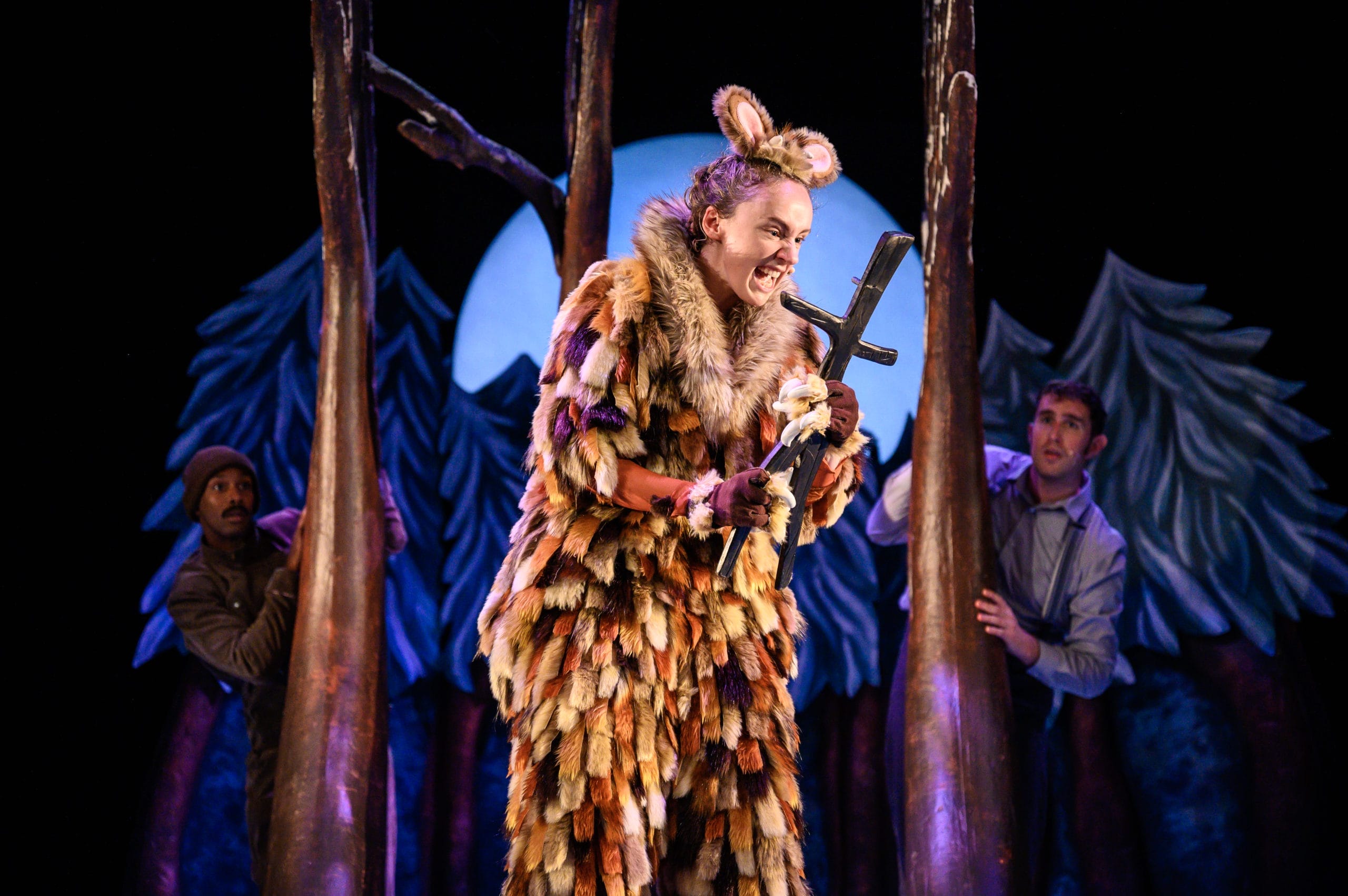 Production shot from The Gruffalo's Child artsdepot! Actor wears a large fluffy gruffalo costume with cute furry areas. She is holding her hazel stick and glaring at it with an exaggerated expression.