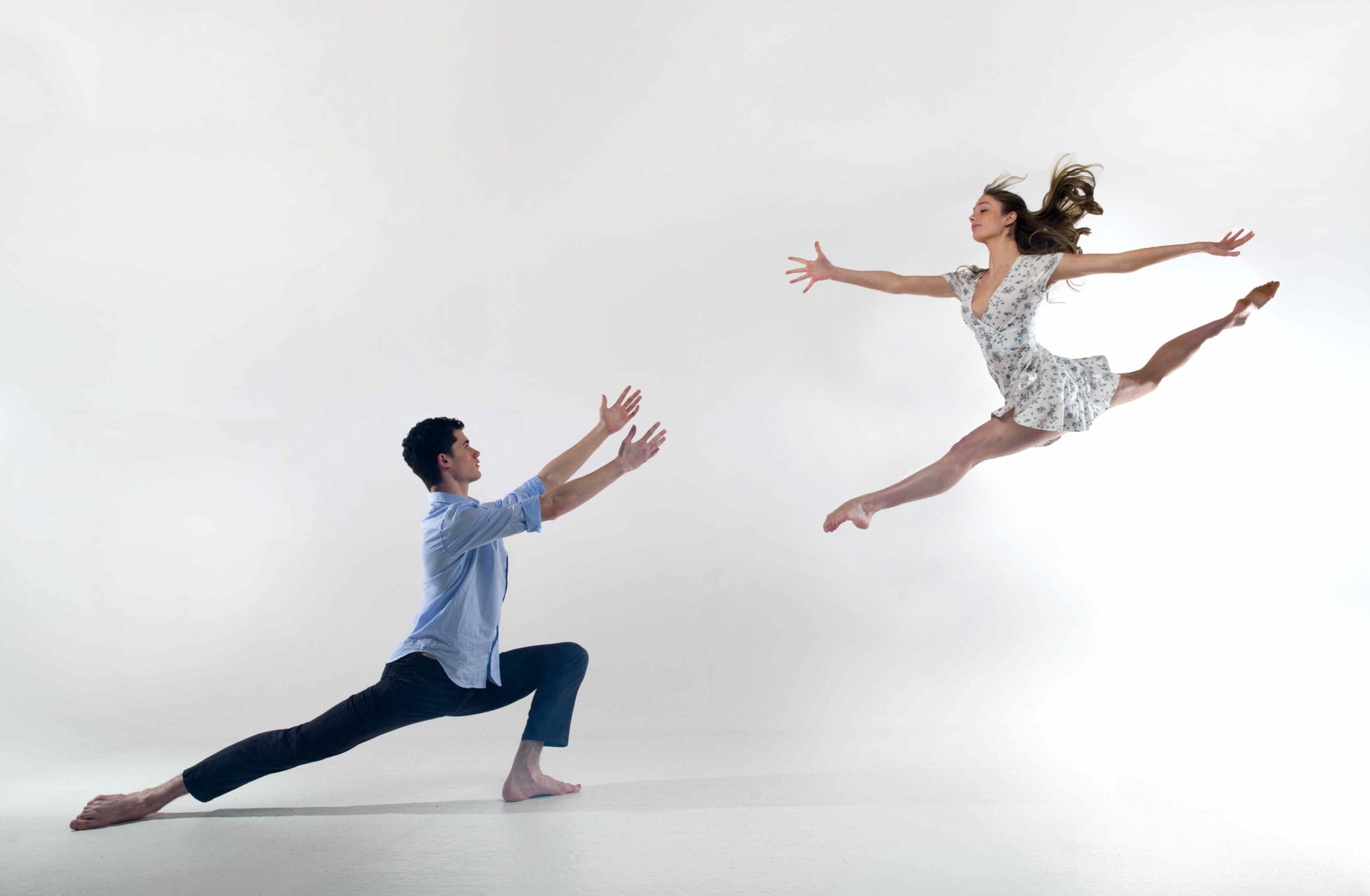 A male and female dancer pose against a white background. The female dancer is mid-leap in a Grand Jeté. The male dancer has outstretched arms, as though reaching for her.