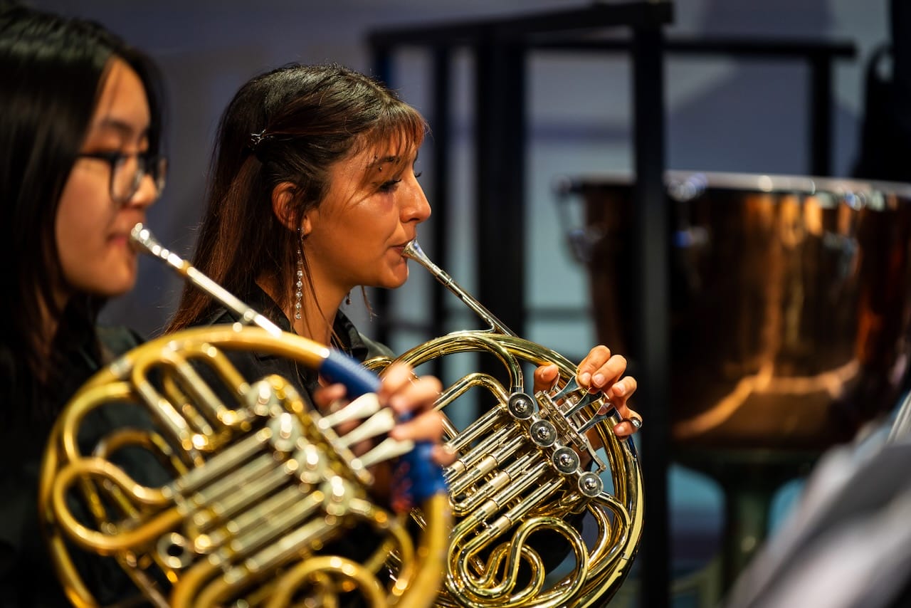 Close up photograph of two female members of London Youth Concert band members, both playing the french horn.