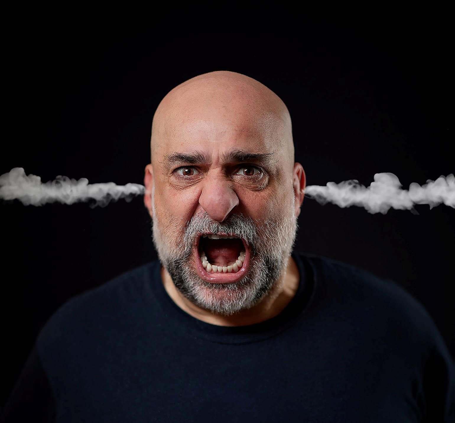 An image of comedian Omid Djalili from the shoulders up. His mouth is open as if shouting and steam is coming out of both of his ears.