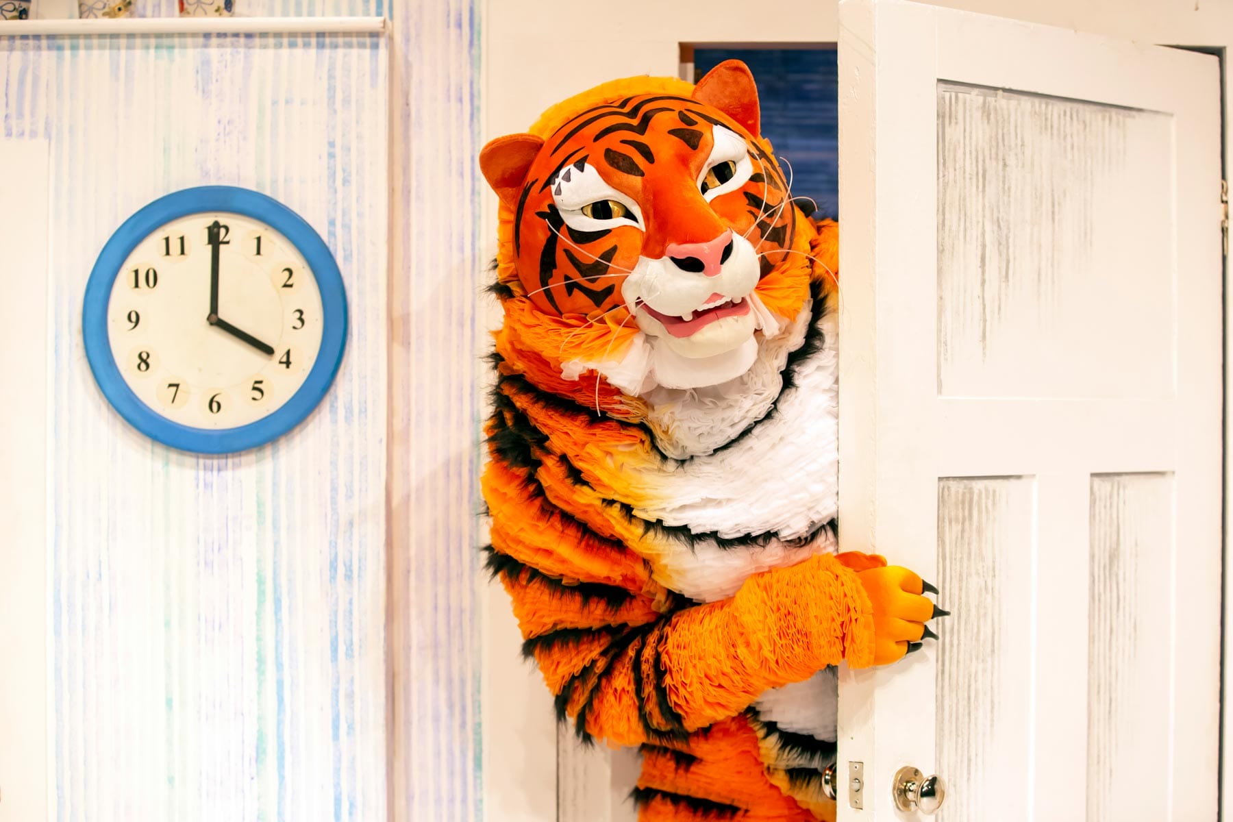 The character of Tiger in The Tiger Who Came to Tea reaches around a white painted door.