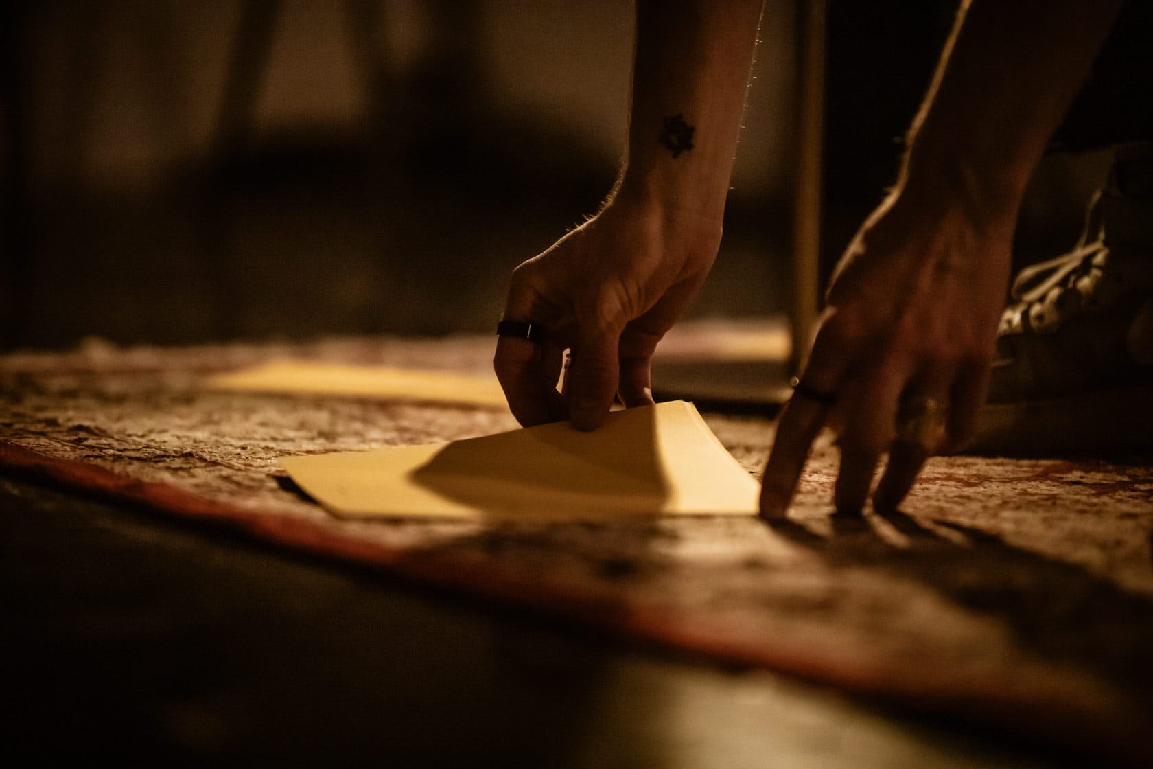 Image shows a pair of hands picking up a piece of paper on a rug.