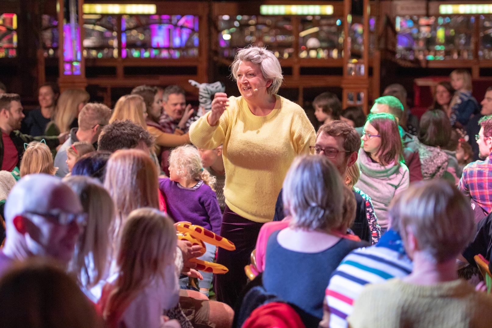 A woman in a yellow jumper is engaging the audience standing in middle of the crowd.