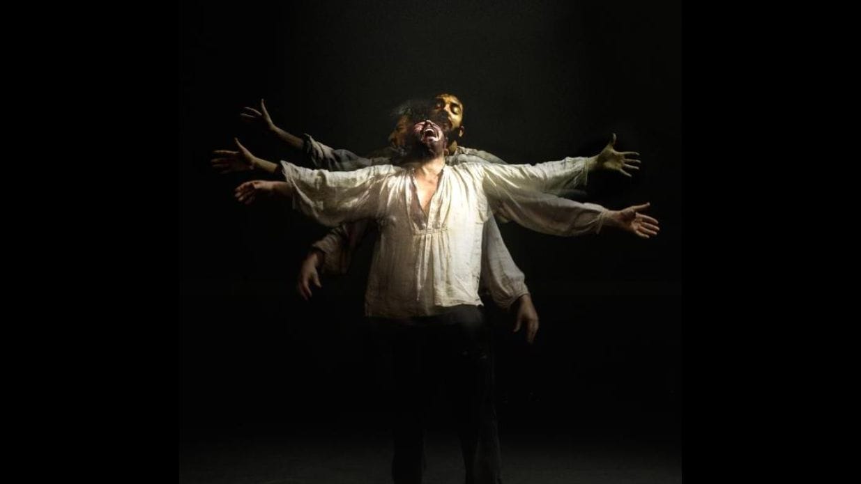 A distorted image of a man in a white shirt standing with his arms raised. He holds a pained expression on his face.