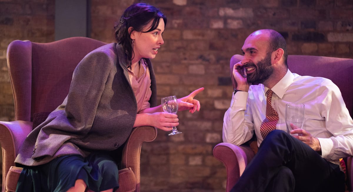 A bearded man in white shirt and tie looking infectiously at the brunette woman speaking to him.