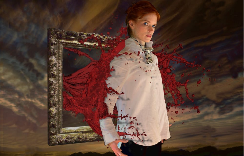 A performer wearing a white shirt stands in front of a gilded picture frame from which blood gushes, splashing against their back.