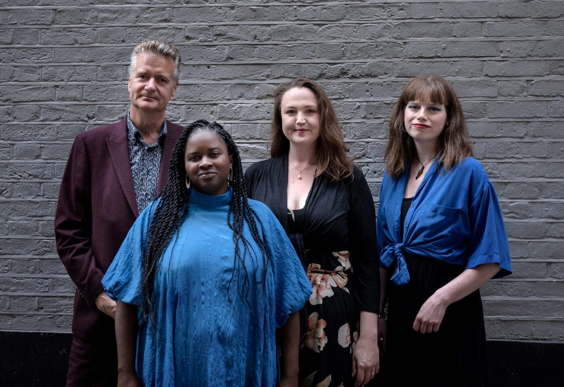 Ineza and the Alex Webb trio are pictured outside, standing in front of a grey brick wall.