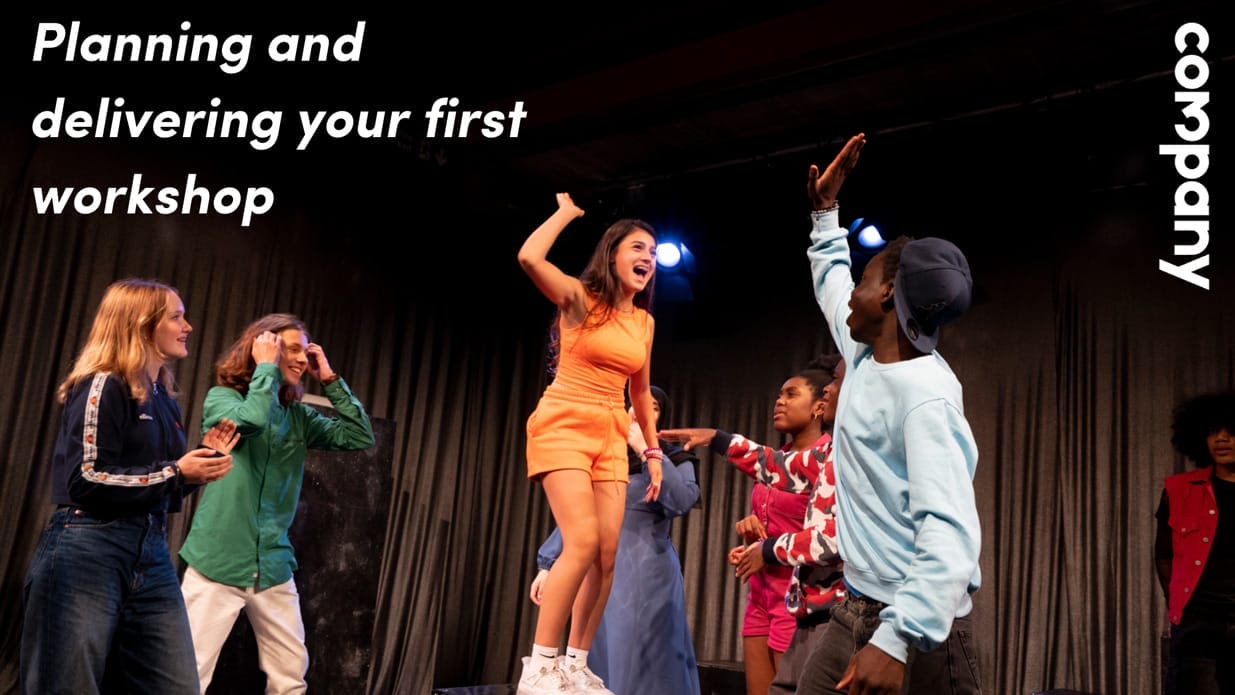 An image from a Company Three performance showing a group of young people on stage. One young person stands on a stool, high-fiving another.