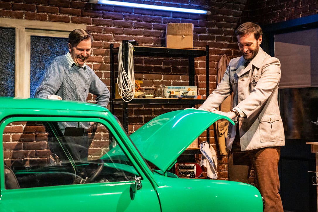 Production photo, two men stand around a green car